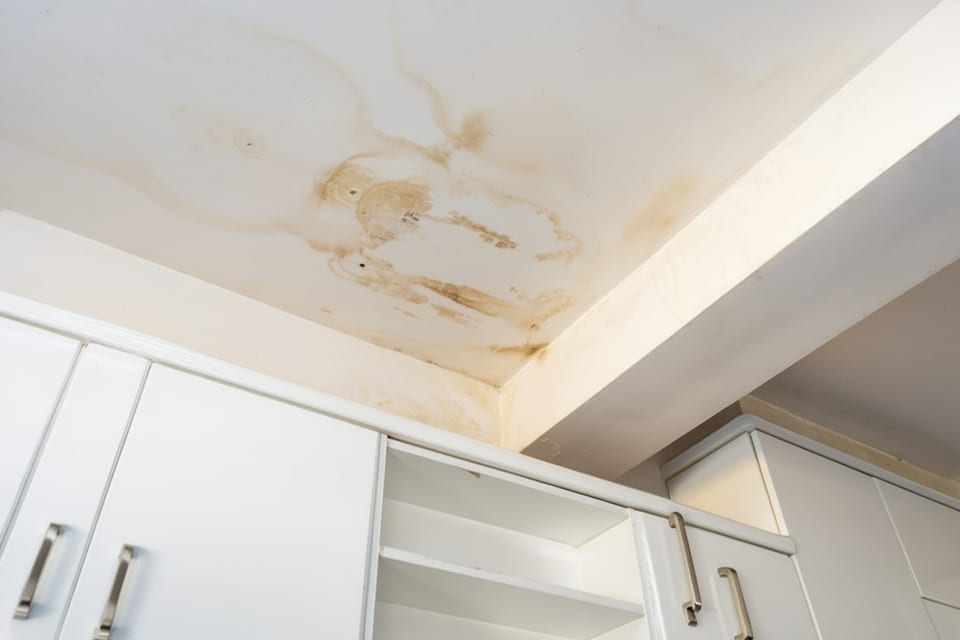 brown water stains spreading across a white ceiling and down the wall above built-in cabinets